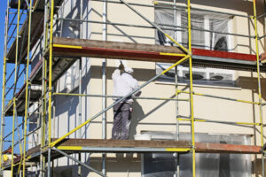 Fachowiec nakłada farbę elewacyjną na fasadę domu
